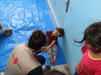 Ein Mädchen sitzt am Boden, ein Mann gibt ihr die Hand.