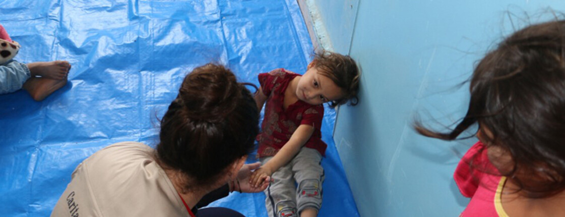 Ein Mädchen sitzt am Boden, ein Mann gibt ihr die Hand.