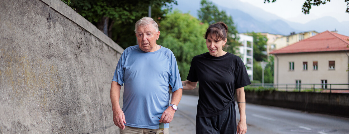 Ein Senior und eine junge Frau gehen gemeinsam entlang einer Straße spazieren.