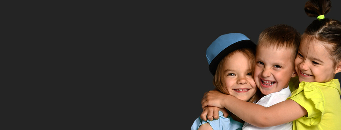 Drei Kinder umarmen sich und lachen in die Kamera, der Hintergrund ist schwarz.