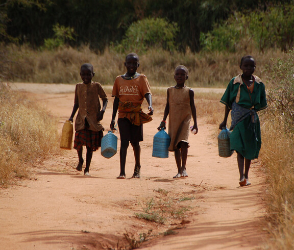Vier Kinder mit vollen Wasserkanistern kommen den Weg entlang zurück.