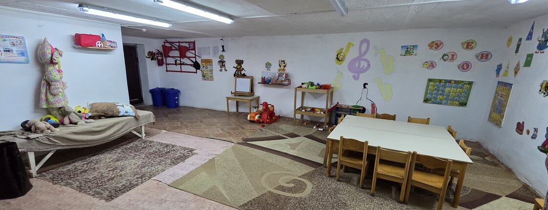 Ein Schutzraum mit Tisch und Sesseln, an den Wänden sind Kinderzeichnungen zu sehen.