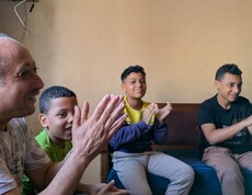 Durch Sing- und Klatschspiele wird das seelische Wohlbefinden der Kinder gefördert.  Ein Mann und vier Kinder klatschen und haben Spaß.