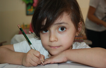 Mädchen sitzt am Tisch und arbeitet mit einem Bleistift.