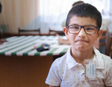 Nahaufnahme eines kleinen jungen mit schwarzen Haaren und Brille, der direkt in die Kamera blickt.