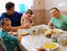 Kinder im Kinderdorf Gomel nehmen gemeinsam mit einem Betreuer ihre Mahlzeiten ein, wobei einige Kinder unterstützt werden.