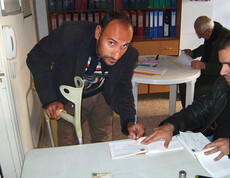 3 Männer in einem engen Raum, einer hat eine Krücke in der Hand