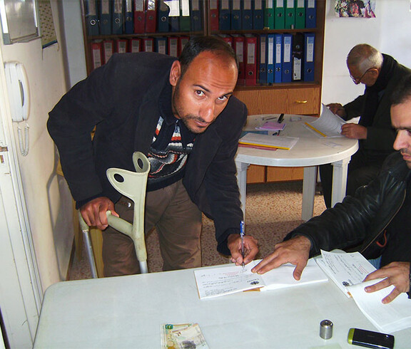 3 Männer in einem engen Raum, einer hat eine Krücke in der Hand