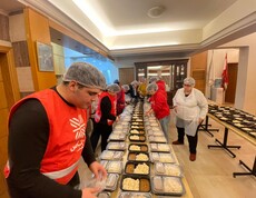 Kolleg*innen der Caritas beim Vorbereiten von Mahlzeiten. Auf einem Tisch vor ihnen sind viele Portionen mit Mahlzeiten.