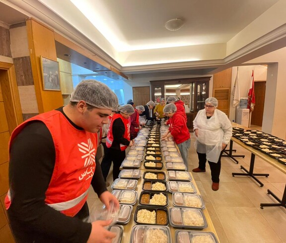 Kolleg*innen der Caritas beim Vorbereiten von Mahlzeiten. Auf einem Tisch vor ihnen sind viele Portionen mit Mahlzeiten.