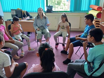 Kinder und eine erwachsene Person sitzen im Sesselkreis und reden