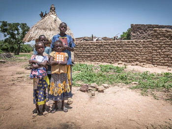 Vier Schulkinder stehen mit Schulheften unter dem Arm vor einem kleinen Haus in Burkina Faso. 