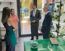 Vier Erwachsene stehen in einem Blumenladen und unterhalten sich, Regale mit Pflanzen und Dekoration sind im Raum sichtbar.