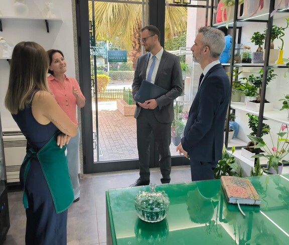 Vier Erwachsene stehen in einem Blumenladen und unterhalten sich, Regale mit Pflanzen und Dekoration sind im Raum sichtbar.