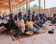 Eine Gruppe südsudanesischer Kinder sitzt am Boden und isst lächelnd