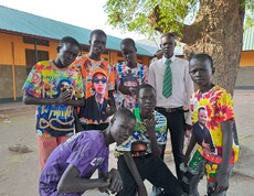 Eine Gruppe junger Südsudanesen posiert unter einem Baum. Alle haben bunte Tshirts an. 