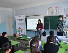 Eine Schülerinnen hält in einem Klassenzimmer eine Präsentation. Sie steht vor einer Power-Point-Präsentation.