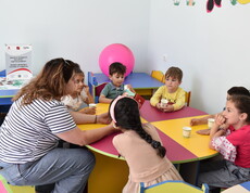 Eine Pädagogin sitzt mit mehreren Kindern an einem Tisch und liest ihnen ein Märchen vor.