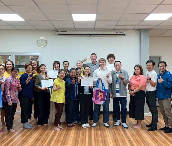 Eine große Gruppe von Menschen steht in einem Raum zusammen und hält Zertifikate in die Kamera.