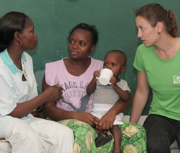 Vier Erwachsene im Gespräch, ein Kleinkind trinkt dabei aus einem Becher auf dem Schoß der Mutter