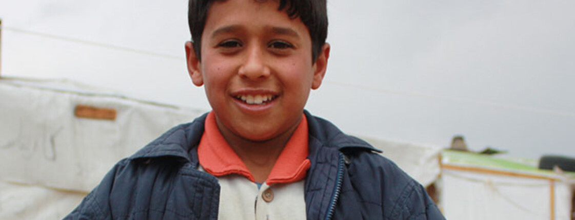 Ein Flüchtlingskind befindet sich im Libanon in einem Zeltlager. Er hält eine große Schachtel in den Händen. 