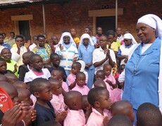 Eine Gruppe burundischer Waisenkinder steht da und schaut zu einer burundischen Ordensschwester am Rand. 