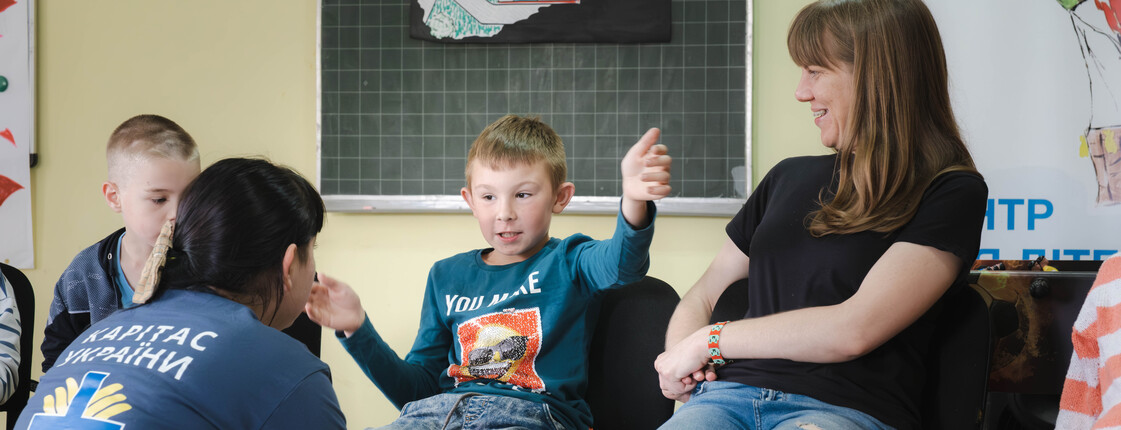 Kleine Kinder und Betreuerinnen sitzen gemeinsam in einem Klassenraum im Sesselkreis.