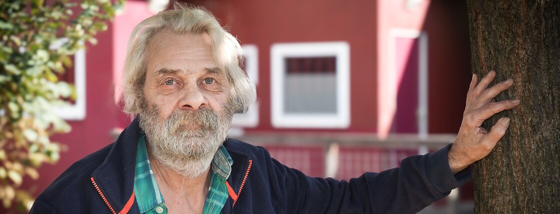 Bewohner des Ressidorfs stützt sich mit der Hand an einem Baum ab