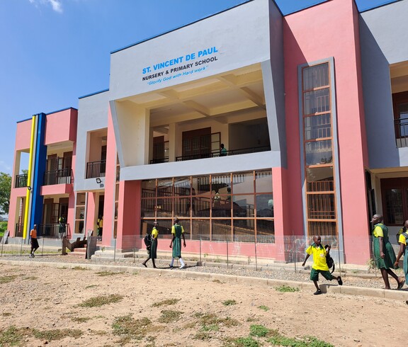 Das neue Schulgebäude von außen, mit freundlichen Farben angemalt und laufenden Schulkindern davor. 