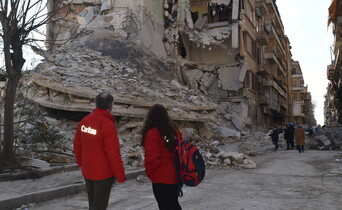 Es sind zwei Personen mit Caritas-Jacken von hinten zu sehen, sie stehen vor Trümmern eines Hauses