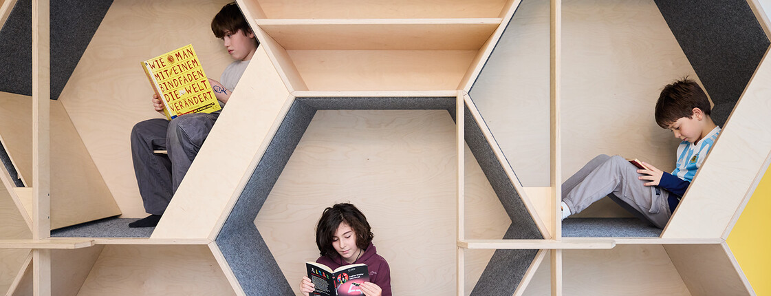 Drei Schüler*innen lesen in modularer Lernecke aus Holz mit individuellen Rückzugsorten