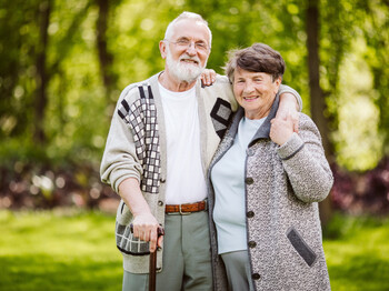 Ein glückliches Paar älteren Alters steht in einem grünen Garten zu einem Portrait zusammen. 