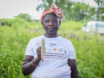 Eine Frau steht auf einem grünen Feld und hält eine Pflanze in der Hand.