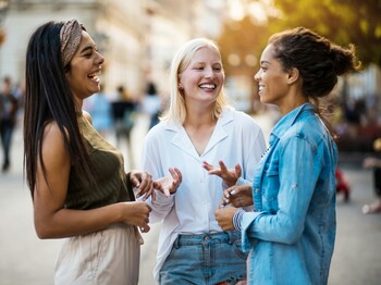Drei lachende Frauen unterschiedlicher Herkunft unterhalten sich.