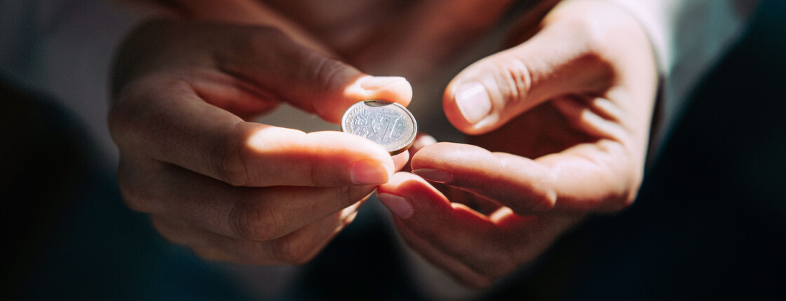 Zwei Hände halten eine Ein-Euro-Münze.