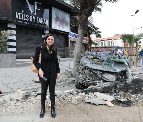 Frau steht auf einer Straße neben einem stark beschädigten Auto und Trümmern.