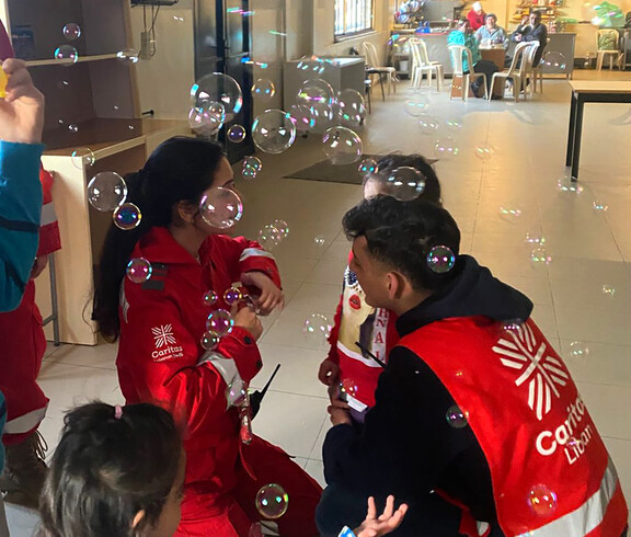 Caritas Mitarbeiter*innen beim Spielen mit Kindern, in der Luft fliegen Seifenblasen.