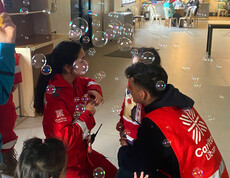 Caritas Mitarbeiter*innen beim Spielen mit Kindern, in der Luft fliegen Seifenblasen.