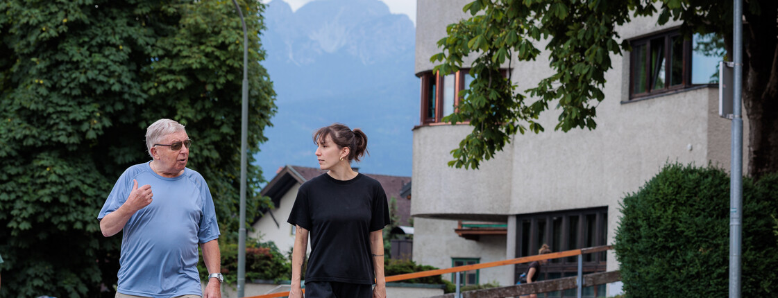 Eine Ehrenamtliche begleitet einen Angehörigen regelmäßig bei Spaziergängen in der Nachbarschaft.