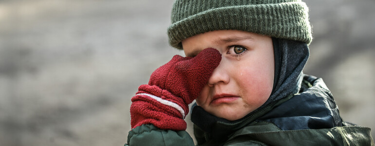 Kind mit Mütze und roten Handschuhen wischt sich weinend die Augen ab