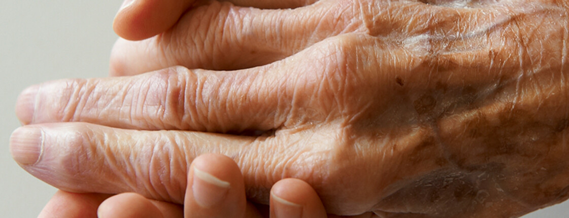 Eine ältere Hand wird sanft von einer anderen Hand gehalten.