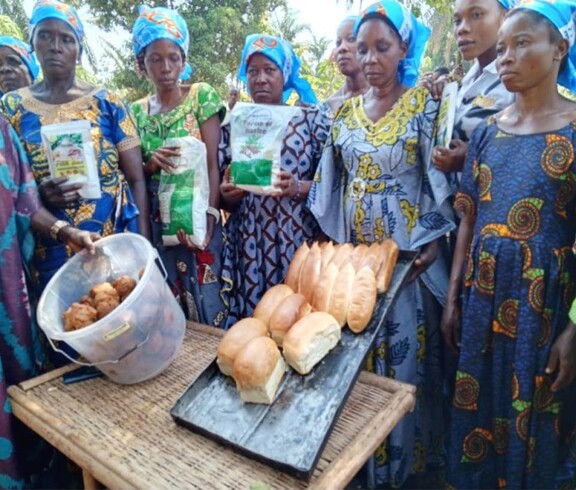 Gruppe von Frauen zeigt gebackenes Brot und Zutaten wie Mehl und Teigbällchen auf einem Tisch im Freien