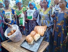 Gruppe von Frauen zeigt gebackenes Brot und Zutaten wie Mehl und Teigbällchen auf einem Tisch im Freien