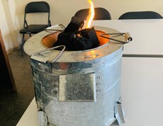 Im Projekt PERDURER kommen Energiesparöfen als saubere Kochalternative zum Einsatz  Metallofen mit brennenden Briketts auf einem Tisch.