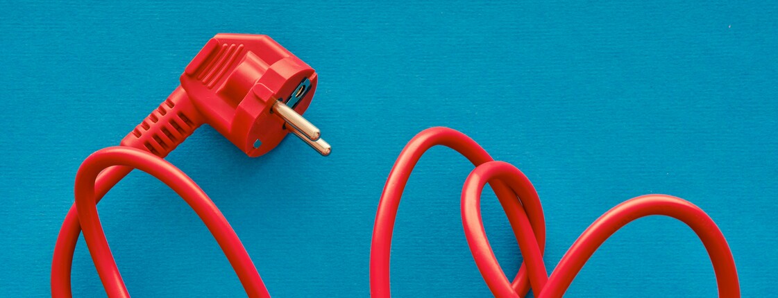 Ein verworrenes, rotes Stromkabel mit Stecker liegt auf einem blauen Hintergrund.