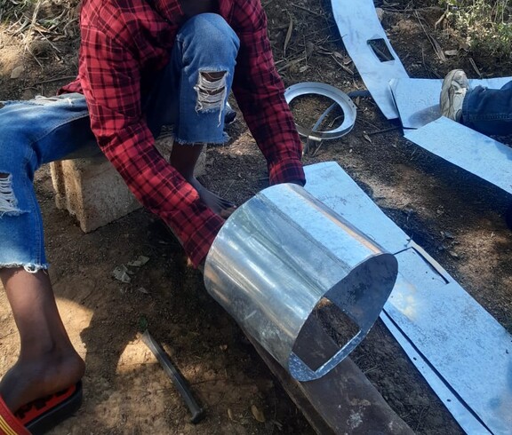 Für einen effizienten und klimafreundlichen Energieeinsatz werden Energiesparöfen aus Metall gefertigt  Ein Mann formt ein rundes Metallblech am Boden zu einem Zylinder.