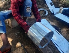 Für einen effizienten und klimafreundlichen Energieeinsatz werden Energiesparöfen aus Metall gefertigt  Ein Mann formt ein rundes Metallblech am Boden zu einem Zylinder.