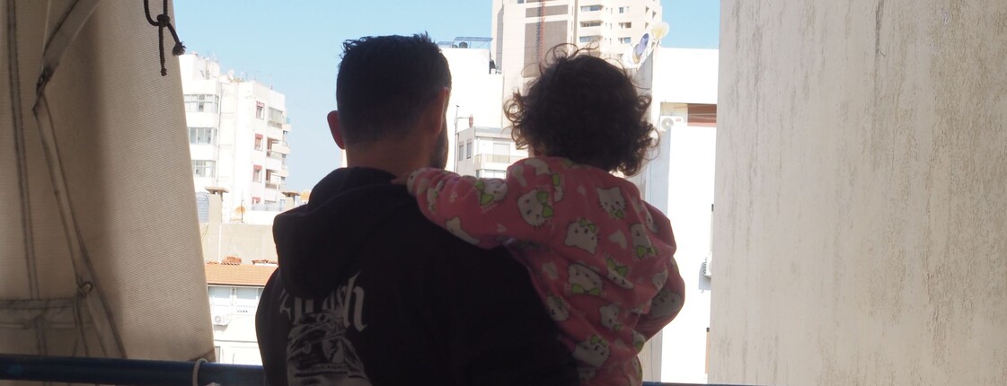 Ein Mann hält ein Kind auf dem Arm und blickt auf die Stadt