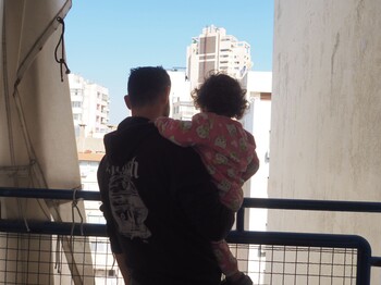 Ein Mann hält ein Kind auf dem Arm und blickt auf die Stadt