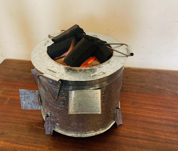 Energiesparofen mit Biokohlebriketts reduziert den Verbrauch herkömmlicher Brennstoffe  Metallofen mit glühenden Briketts auf einem Holztisch.